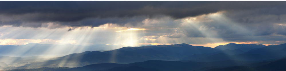 Image of sky and mountain range with sun peering through clouds